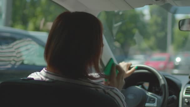 30-as éveiben járó nő autót vezet a városi dugóban és mobiltelefonnal beszél. Veszélyes vezetés egy cellában. Autós telefonhívás kéz nélkül ingyenes felszerelés. — Stock videók