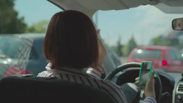 30s woman driving car and holding mobile phone in hands. Female driver holding steering wheel and using cell phone for online map application. — Stock Video