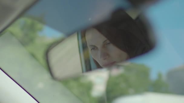 Car mirror reflection of young adult woman driving car in city. Inside view of female driver looking around. — Stock Video