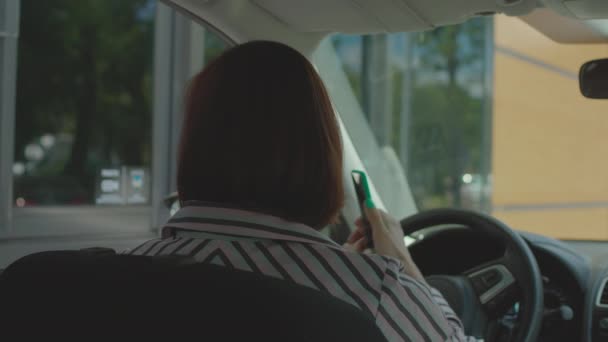 Conductor adulto joven pidiendo comida rápida, pagando la factura con teléfono móvil y terminal sin contacto sentado en el coche. Mujer usando el pago de NFC en su celular en el restaurante de comida rápida. — Vídeos de Stock