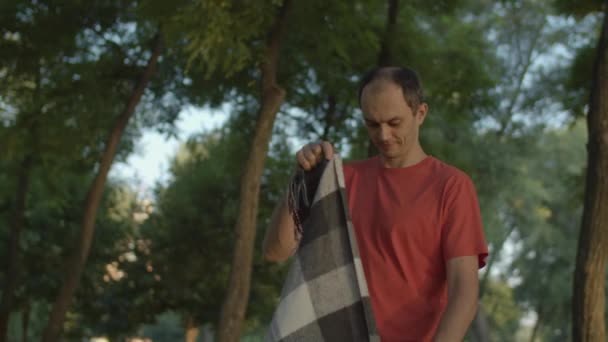 Een dertiger man die deken verspreidt voor de picknick met een geliefde vrouw in het stadspark. gelukkig familie voorbereiding plaats voor picknick samen. — Stockvideo