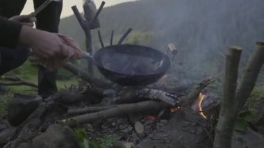 Dağ kampında erkek el yemeği, şenlik ateşinde pişiyor. Dışarıda ateş yakmak..