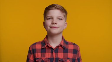 Neşeli genç bir çocuk doğrudan kameraya bakarken başparmağını kaldırıyor. Parlak sarı arka plan, onun kendine güvenen ve mutlu ifadesine enerji ve pozitiflik katıyor..