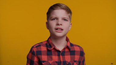 Genç bir çocuk L şeklini alıyor. Parmakları alnında ve muzip bir şekilde Ezik diyor. Onun ifadesi parlak sarı arka plana karşı kendinden emin ve haylaz.