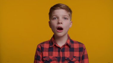 Genç bir çocuk ağzı açık durur, şok ya da şaşkınlık belirtileri gösterir. Geniş gözleri ve dramatik tepkisi parlak sarı arka plana çarpıyor..