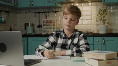 Evdeki not defterine notlar yazarken online bir derse katılan genç bir çocuk..