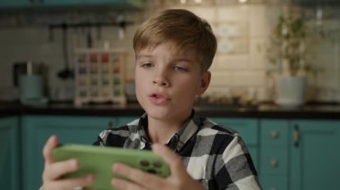 Evde akıllı telefonuyla video oyunu oynayan genç bir çocuk var..