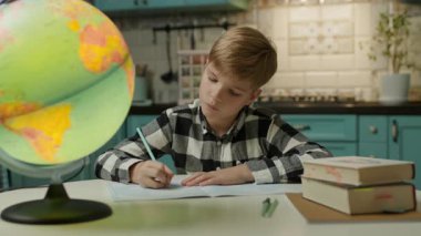 Evde ders çalışan, coğrafya veya okul ödevleri için bir küreye bakarken ev ödevi yapan odaklanmış bir çocuk..