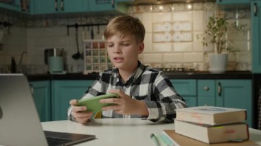 Bir okul çocuğu evde oturup ev ödevini ihmal ederken akıllı telefonuna odaklanır ve mobil oyunlar oynar..