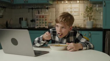 Genç çocuk evde dizüstü bilgisayar izlerken mısır gevreği yiyor, rahat bir kahvaltı yapıyor ve evde dinleniyor.