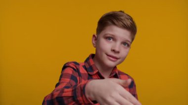 Genç bir çocuk hoş geldin jesti ile elini sallıyor, neşeli görünürken birini içeri davet ediyor. Parlak sarı arka plan onun dostça ve açık ifadesini vurguluyor..