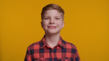 Neşeli bir çocuk doğrudan kameraya bakarken başparmağını kaldırıyor. Parlak sarı arka plan, onun kendine güvenen ve mutlu ifadesine enerji ve pozitiflik katıyor..