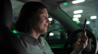 Neşeli kadın güvenli bir şekilde park etmiş arabasında oturuyor, elinde akıllı bir telefonla görüntülü konuşma sırasında konuşuyor, sıradan bir şehir hayatı..
