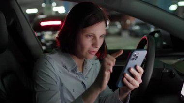 30 'lu yaşlarında gülümseyen bir kadın park halindeki bir arabada oturuyor ve cep telefonuyla mesaj atıyor, rahat ve rahat bir şekilde..