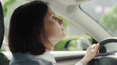 30 'lu yaşlarında araba süren bir kadının yakın çekimi, elleri direksiyonda ve odaklanmış bir yüz ifadesi, yolda bir anlık konsantrasyon yakalamış..