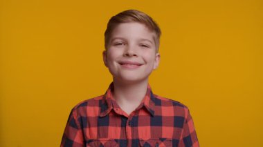 Neşeli bir çocuk doğrudan kameraya bakarken başparmağını kaldırıyor. Parlak sarı arka plan, onun kendine güvenen ve mutlu ifadesine enerji ve pozitiflik katıyor..