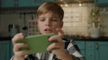 Evde akıllı telefonuyla video oyunu oynayan genç bir çocuk var..