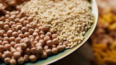 Ekmek, pirinç, kepekli taneler, yulaf, buğday ve mısır makarnası da dahil olmak üzere çeşitli karbonhidrat zengini yiyecekler bir tabakta sergilenmekte ve ahşap bir masada dönmektedir. Beslenme ve sağlıklı beslenme için mükemmel.