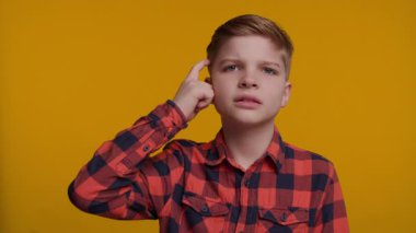 Genç bir çocuk parmağıyla şakağına hafifçe vuruyor, önce düşünmesi gerektiğini işaret ediyor. Onun düşünceli ifadesi parlak sarı arka planla çelişiyor, zekayı ve karar verme mekanizmasını vurguluyor..