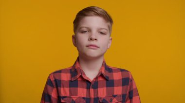 Genç bir çocuk üzgün bir ifadeyle kameraya bakar, derin bir duygu aktarır. Parlak sarı arka plan onun ruh haliyle çelişiyor, duygularını ve yüz ifadesini vurguluyor..