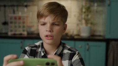 Evde akıllı telefonuyla video oyunu oynayan genç bir çocuk var..