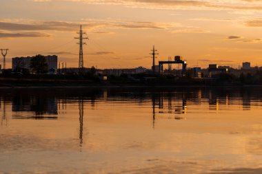 Günbatımında turuncu renklerle sakin su nehri gölünde sanayi bölgesi yansıması
