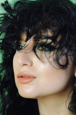 Dumanlı. Parlak makyajlı ve kıvırcık saçlı güzel bir esmer manken. Moda ve güzellik, kozmetik kullanarak. Göz farı ve rujun canlı renkleri. Salon, makyaj sanatçısı, beyaz model..