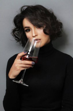 Parlak makyajlı ve kıvırcık saçlı güzel bir esmer manken. Moda ve güzellik, kozmetik kullanarak. Göz farı ve rujun canlı renkleri. Salon, makyaj sanatçısı, beyaz model. Şarap içiyorum..