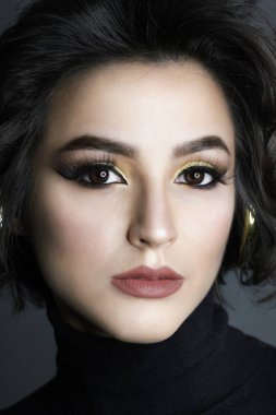 Parlak makyajlı ve kıvırcık saçlı güzel bir esmer manken. Moda ve güzellik, kozmetik kullanarak. Göz farı ve rujun canlı renkleri. Salon, makyaj sanatçısı, beyaz model..