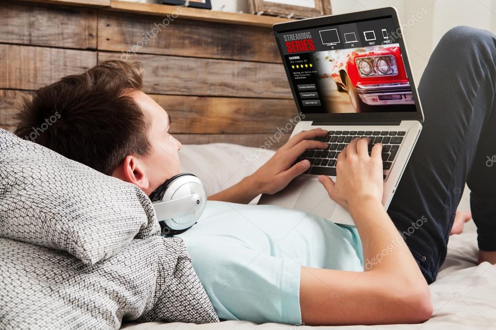 Man watching streaming series in a laptop computer, lying in the bed.