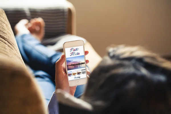 Mujer usando filtros de fotos en un teléfono móvil mientras está acostada en un sofá . — Foto de Stock