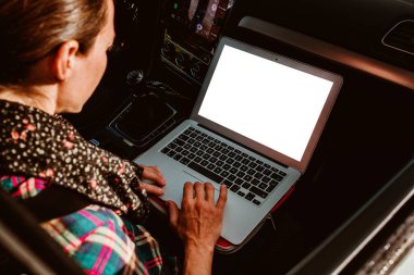 Kadın arabanın içinde dizüstü bilgisayar kullanıyor, yardımcı pilot koltuğunda..