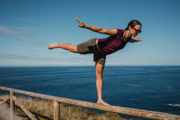 在海岸边的木栏杆上行走和保持平衡的女人 — 图库照片
