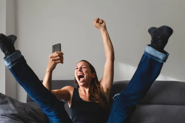 Vit Kvinna Sitter Soffan Reagerar Överlycklig Och Upphetsad Till Mobiltelefon Stockfoto