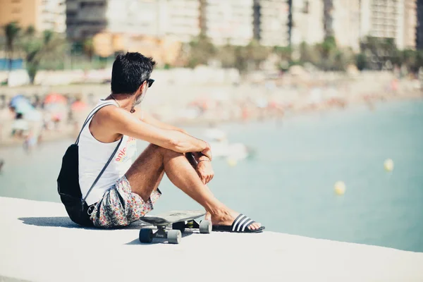 Man sitting at the border of the coast, with a skate. — Stock Photo, Image