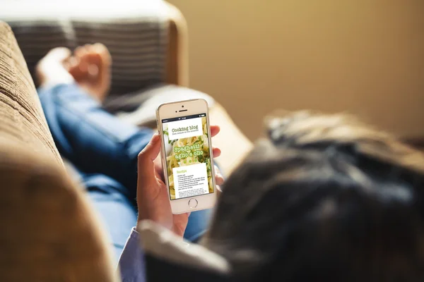 Kvinna läser hennes mobiltelefon, matlagning blogg på skärmen. Stockfoto