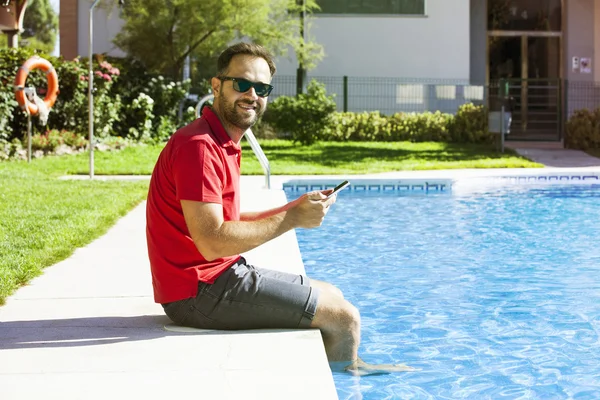 Hombre usando la tableta sentada en la piscina . — Foto de Stock
