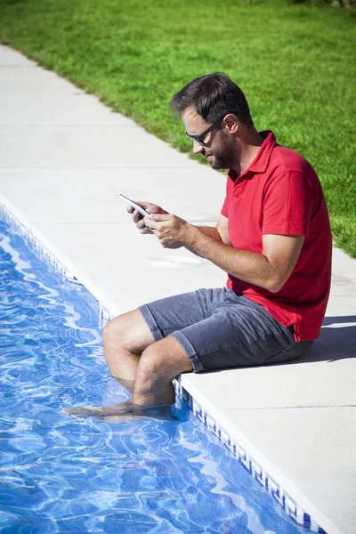 Hombre leyendo tableta sentado en la piscina . —  Fotos de Stock