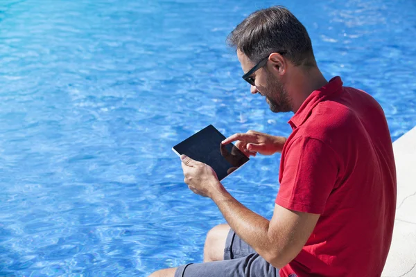 Hombre usando la tableta sentada en la piscina . —  Fotos de Stock