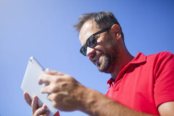 Un hombre sonriente leyendo las noticias en una tableta. Fondo cielo azul . —  Fotos de Stock