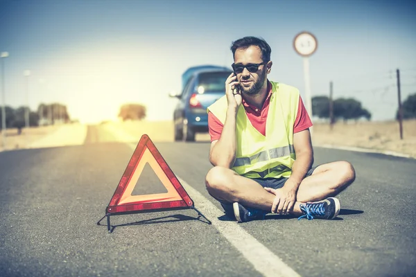 Uomo seduto a parlare per telefono in mezzo alla strada dopo un guasto alla macchina . — Foto Stock