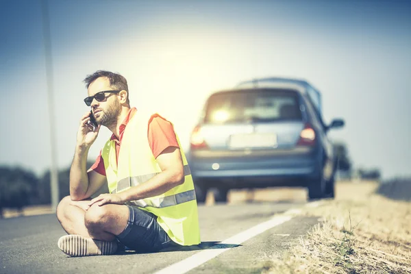 Homem sentado na estrada, conversando por telefone após um colapso do carro . — Fotografia de Stock