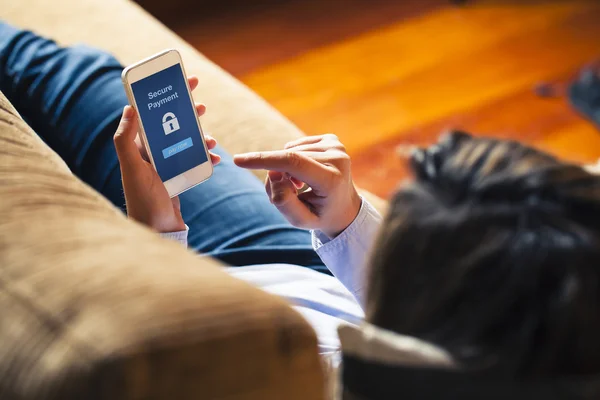Mujer que usa el móvil para pagar mientras está acostada en un sofá en casa. Pantalla azul . — Foto de Stock