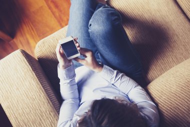 Bir kız bir kanepede otururken bir telefon okuma havadan görünümü.