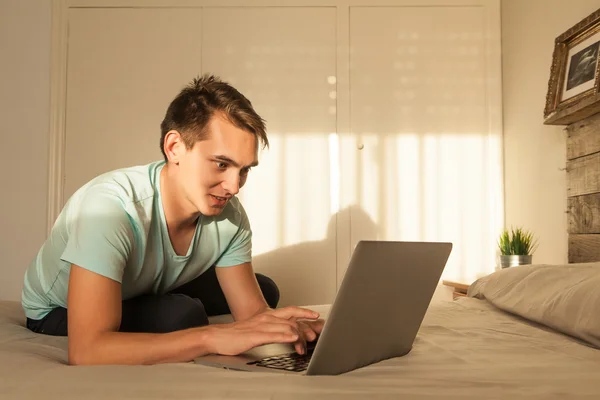 Sonriente joven rubio usando un portátil en el dormitorio . — Foto de Stock