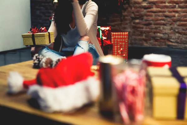 Regalos de Navidad en una mesa con una mujer sentada en el suelo en el fondo . —  Fotos de Stock