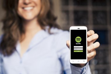 Malaga, İspanya - 26 Nisan 2015: App Spotify cep telefonuyla ekrandaki tutan gülümseyen kadın.