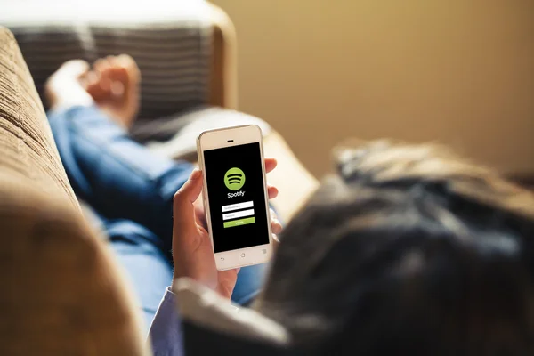 Malaga, spanien - 26. april 2015: spotify-app in einem mobilen bildschirm halten von frau, während sie zu Hause auf einem sofa liegt. — Stockfoto