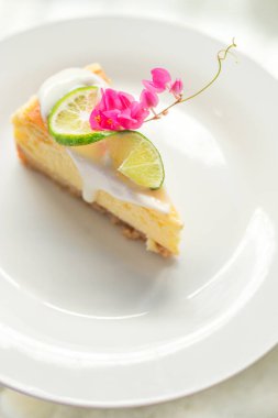 Slice of Lemon Cheesecake on white plate decorated with lemon fresh and flowers