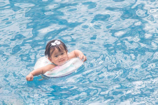 Asian baby eight months swimming with swim ring in pool on summer day